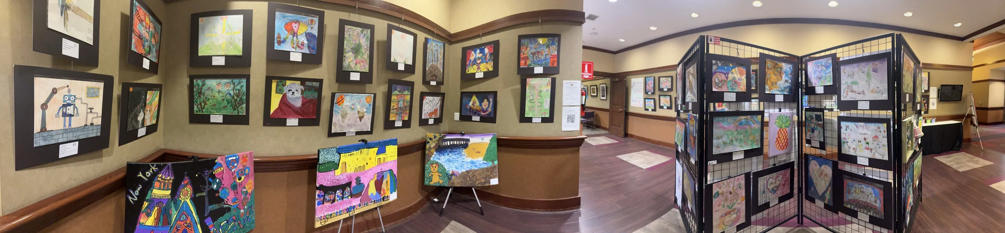Panorama of the exhibition hall, its long walls hung edge to edge with framed student artwork.